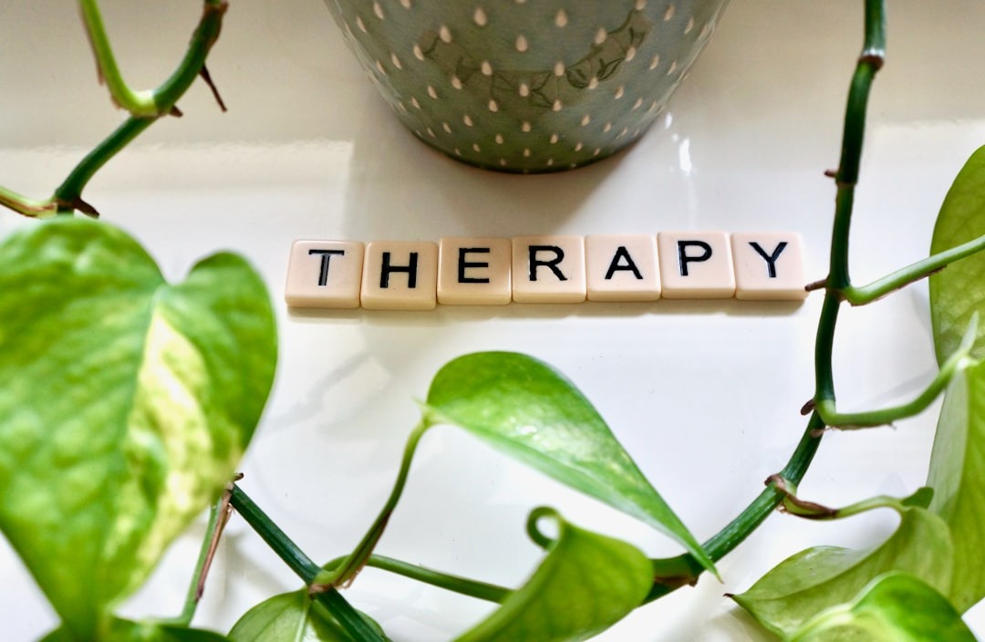 Scrabble tiles spelling therapy placed on a white surface with greenery.
